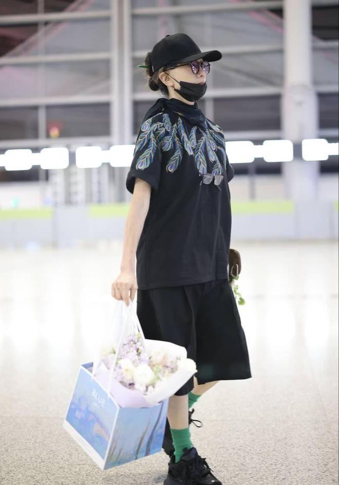 杨丽萍手提鲜花现身机场 穿孔雀翎图案套装超抢眼(图1)