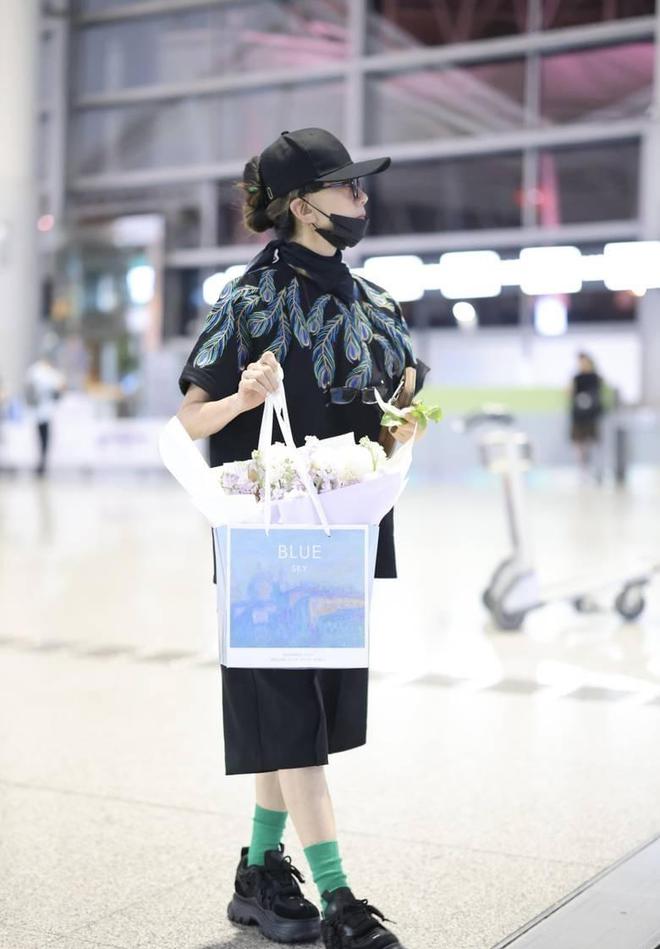 杨丽萍手提鲜花现身机场 穿孔雀翎图案套装超抢眼(图2)